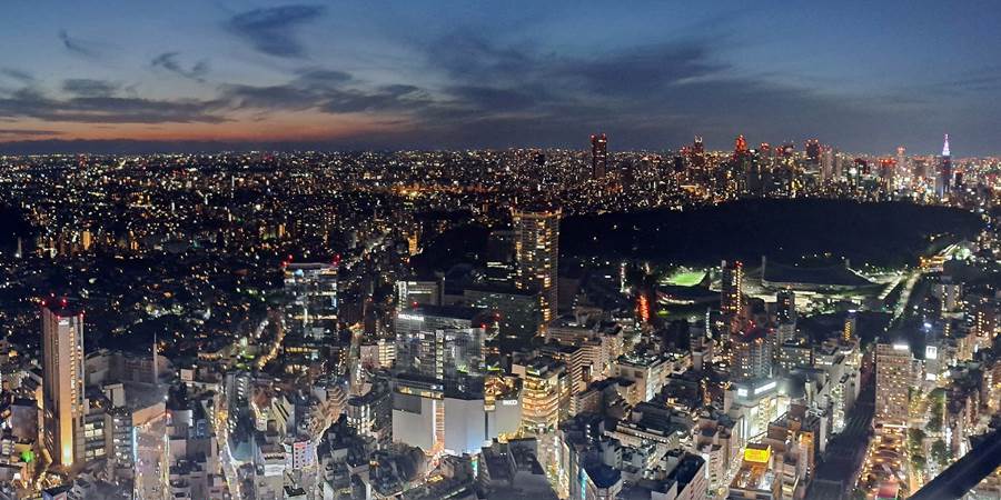 A cityscape at night with a hill and a city in the distance